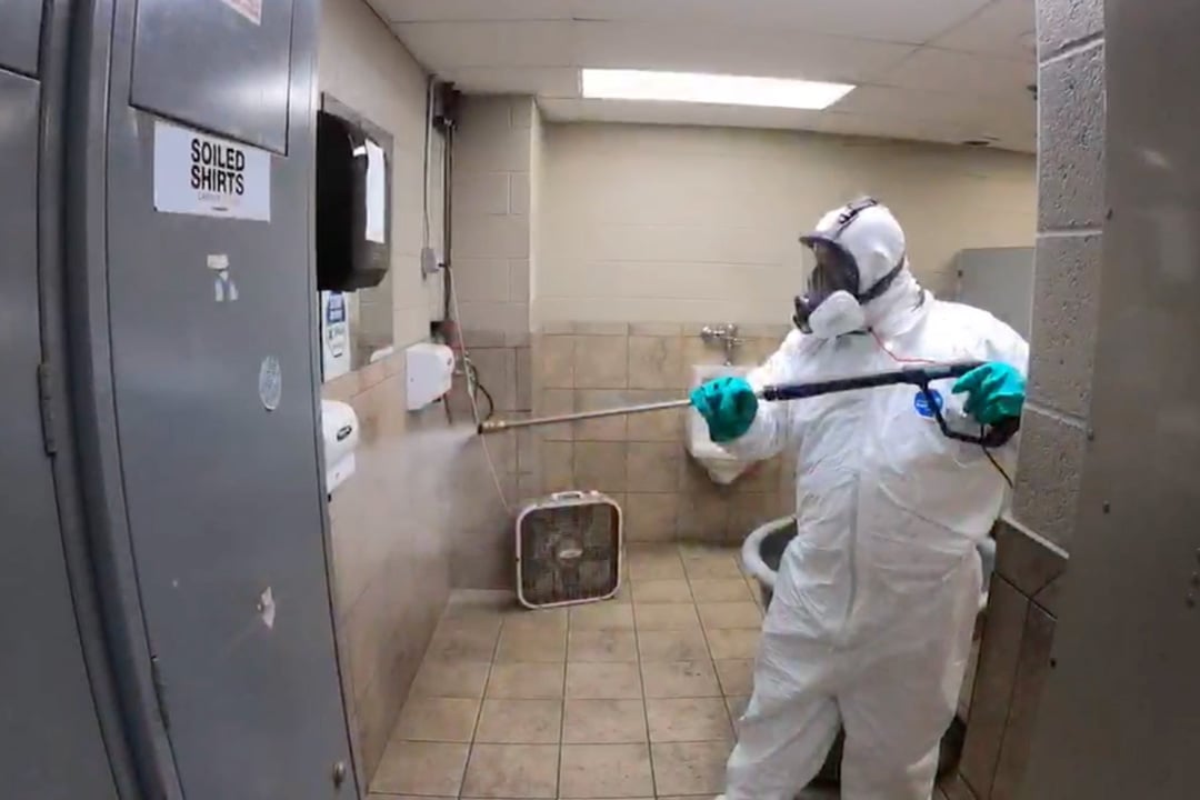 man in PPE applying disinfectant to bathroom