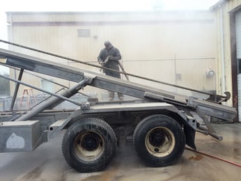 man performing abrasive blasting on a large industrial vehicle