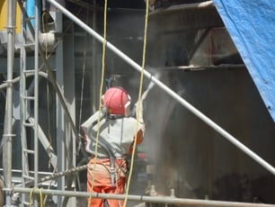 man performing abrasive blasting in a refinery