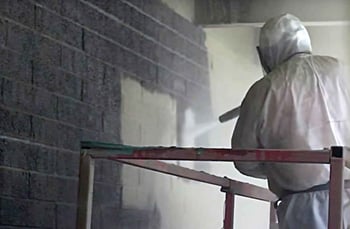 man in safety equipment blasting a cinderblock wall