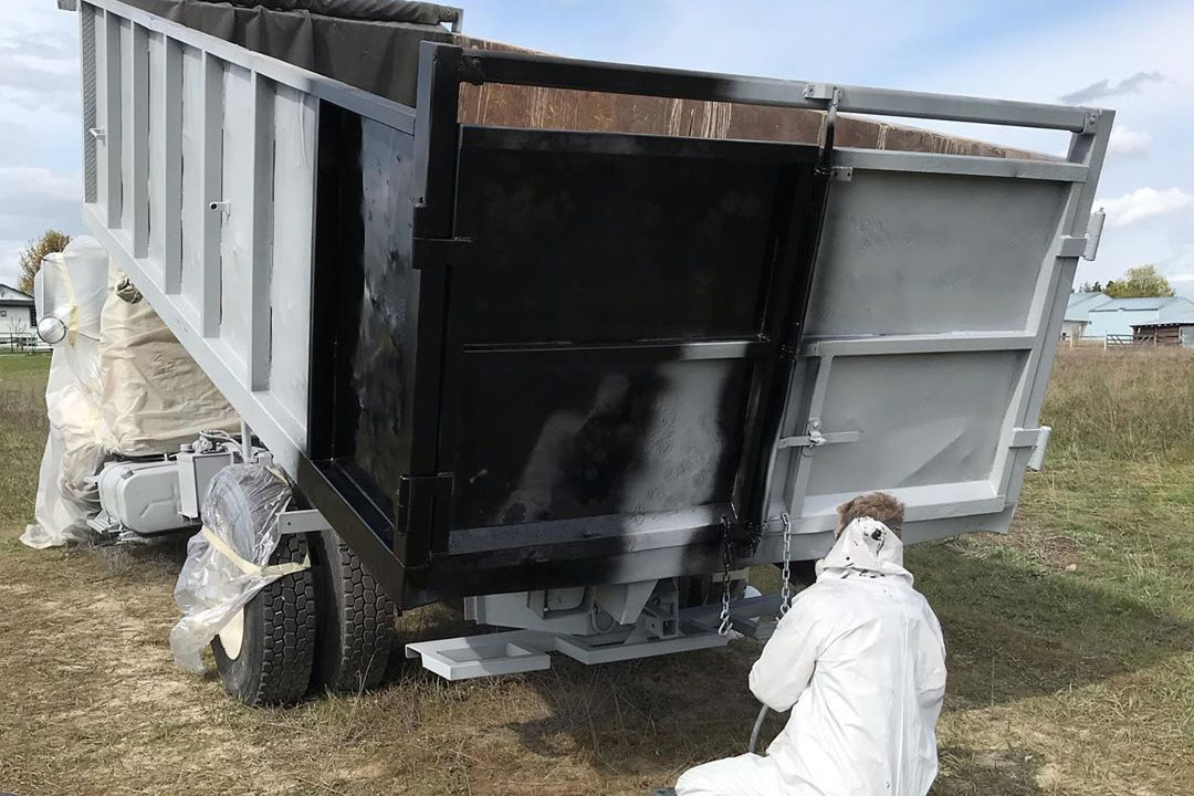 man applying black paint to a freshly blasted dump bed