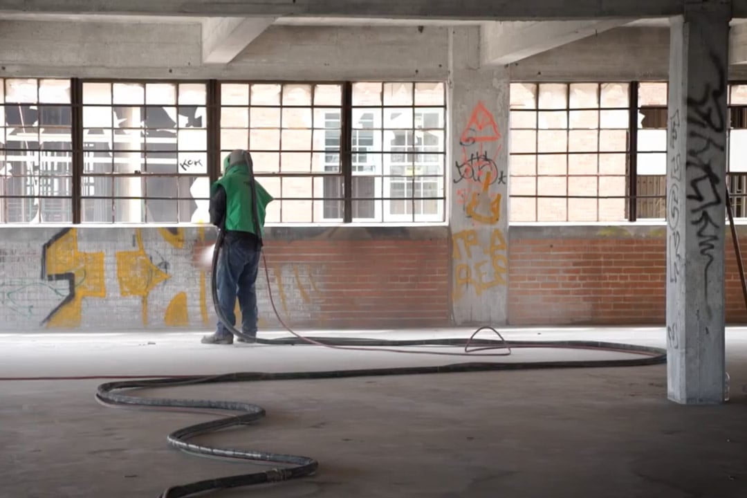 man in green respirator removing graffiti in a brick building