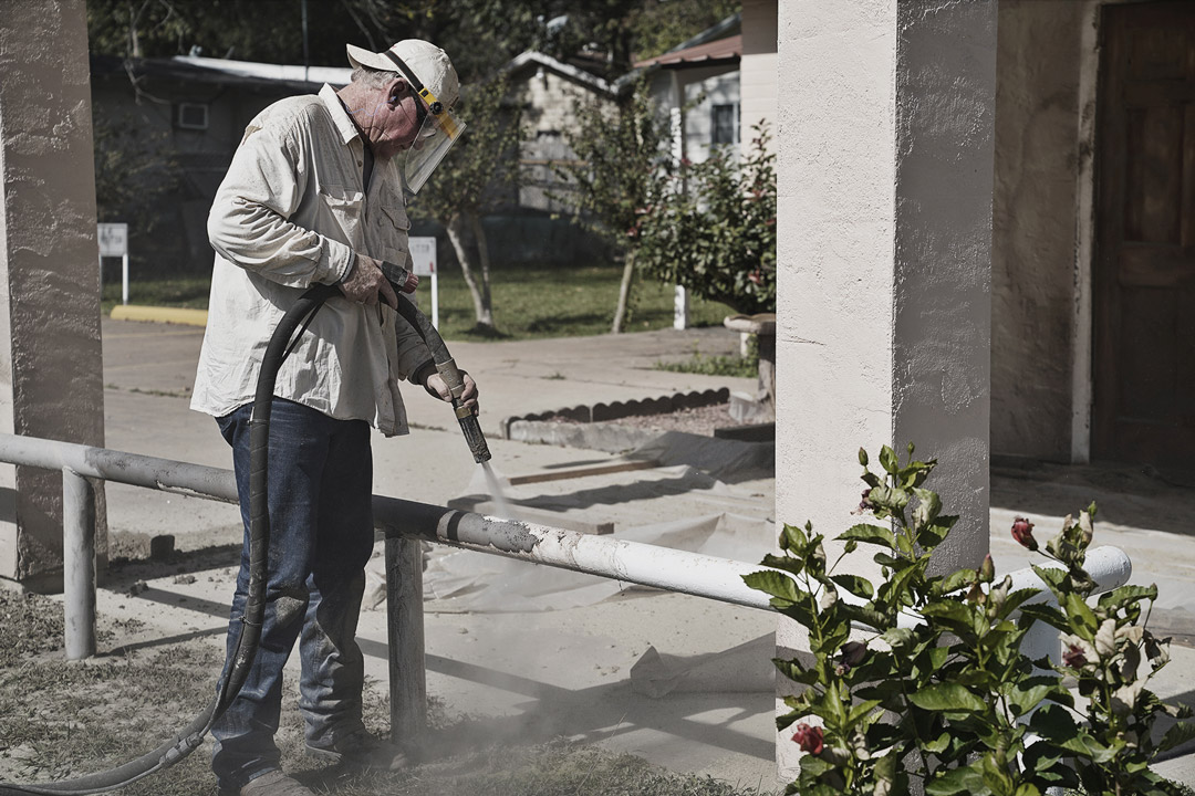 man sandblasting white paint from metal rail