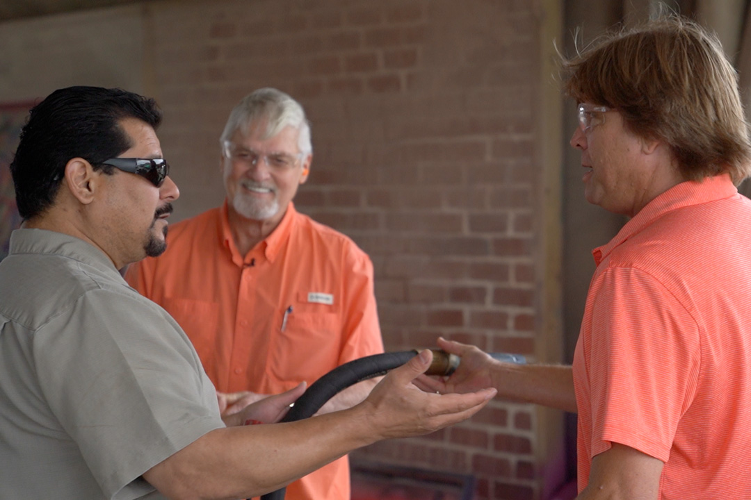 three men talking and holding sandblasting hose