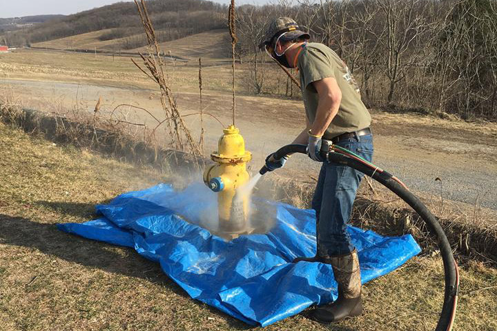 stripping yellow paint from fire hydrant with sandblasting