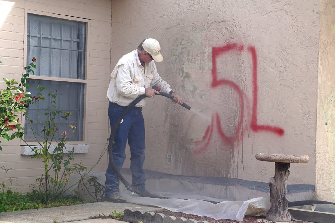 man removing graffiti from exterior wall of church