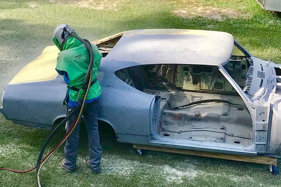 man in green respirator removing paint from a 1969 chevelle