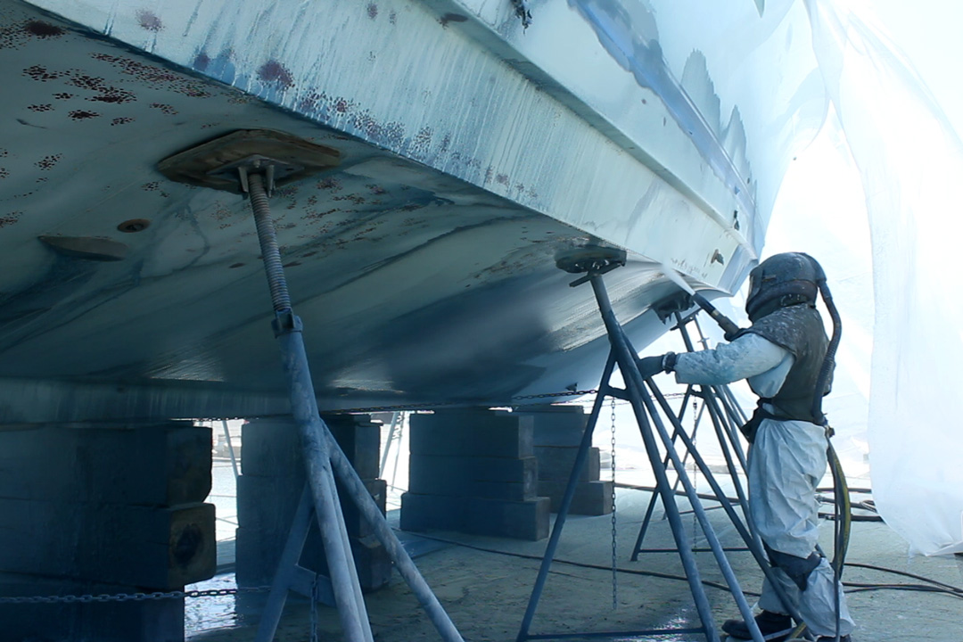 man in respirator removing paint from boat hull