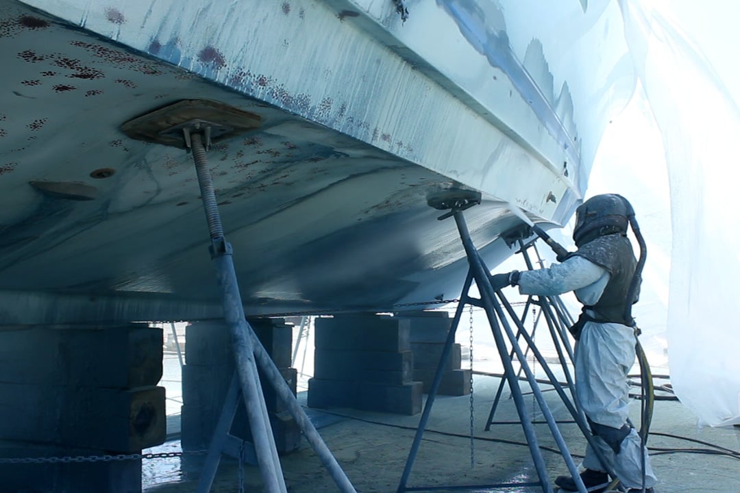 man in respirator blasting away paint on boat